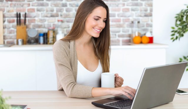 Beautiful young woman using her laptop in the kitchen.